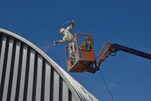 27931152 - tradesman spray painting the roof of an industrial building